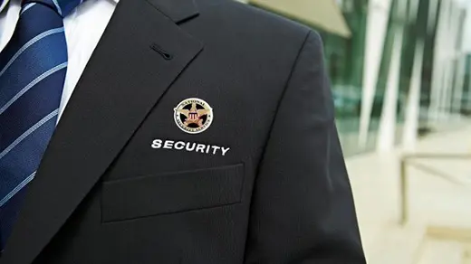 A man in a suit and tie with a badge on his lapel. He is wearing a black jacket