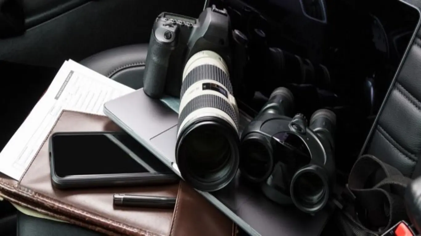 A camera, laptop and binoculars on the seat of a car. 